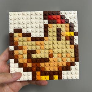 Op de afbeelding: Een pixel art-moza&iuml;ek van een bruine en gele kip gemaakt met kleine vierkante plastic blokken. De kip kijkt naar rechts en heeft een rode kam.