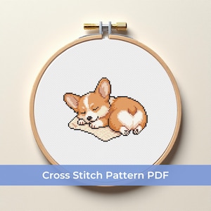 May include: A cross-stitch pattern of a sleeping corgi dog, featuring brown and white fur, resting on a small beige pillow. The design is displayed within a wooden embroidery hoop. The text "Cross Stitch Pattern PDF" is at the bottom.