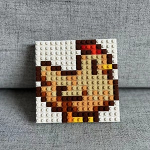 Op de afbeelding: Een bruine en gele kip gemaakt van Lego-stenen. De kip staat op een witte basis.