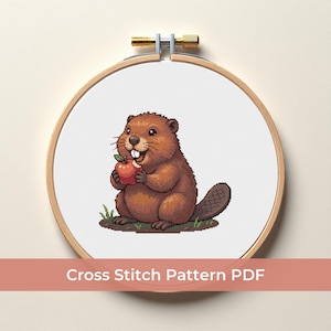May include: A cross-stitch pattern of a cartoon beaver holding a red apple, set within a wooden embroidery hoop. The beaver is brown with a happy expression. The text "Cross Stitch Pattern PDF" is displayed below the hoop.