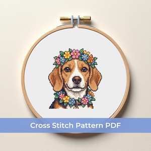 May include: A cross-stitch pattern of a beagle wearing a floral crown and necklace, set in a wooden embroidery hoop. The beagle has brown and white fur. The text "Cross Stitch Pattern PDF" is displayed below the hoop.
