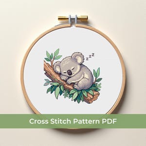 Puede incluir: Patrón de punto de cruz de un koala durmiendo en una rama, rodeado de hojas verdes. El koala es gris y el diseño está en un bastidor de bordado de madera. El texto en la parte inferior dice "Cross Stitch Pattern PDF".