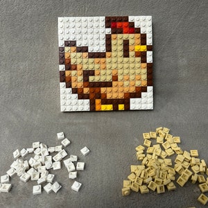 Op de afbeelding: Een close-up van een moza&iuml;ek van een kip gemaakt met kleine plastic blokken. De kip is bruin, geel en rood. Er zijn stapels witte en lichtbruine blokken onder het moza&iuml;ek.