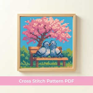 Puede incluir: Un patrón de punto de cruz enmarcado con dos palomas azules posadas en un banco de parque bajo un árbol de flores rosas. El fondo es un cielo azul y hierba verde. El texto "Cross Stitch Pattern PDF" está en la parte inferior.