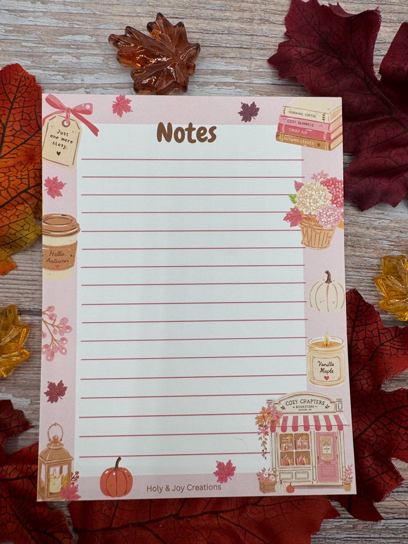 Peut inclure: Un bloc-notes rectangulaire avec des lignes horizontales et le mot Notes en haut. La bordure pr&eacute;sente des illustrations de livres, une tasse de caf&eacute; marqu&eacute;e Hello Autumn, une citrouille, une bougie marqu&eacute;e Vanilla Maple et une boutique Cozy Chapters.