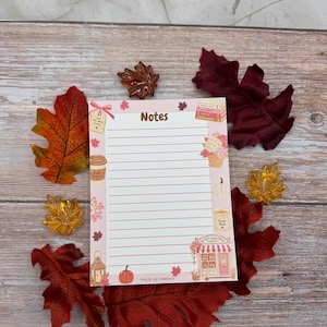 May include: A rectangular notepad with horizontal lines and the word Notes at the top. The border features illustrations of a coffee cup, a pumpkin, a candle, a lantern, a bookstore, and autumn leaves. The text Holy & Joy Creations is at the bottom.