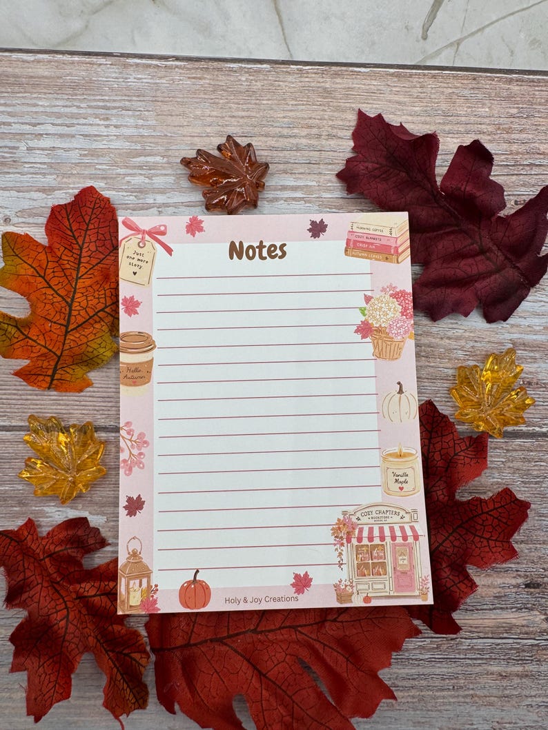 Peut inclure: Un bloc-notes rectangulaire avec des lignes horizontales et le mot Notes en haut. La bordure pr&eacute;sente des illustrations de livres, une tasse de caf&eacute;, une citrouille, une bougie, une lanterne et une boutique nomm&eacute;e Cozy Chapters. Le texte Holy & Joy Creations est en bas.
