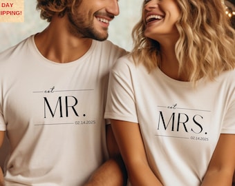 May include: Two white t-shirts with black text. The text on the left shirt reads "est. MR. 02.14.2025". The text on the right shirt reads "est. MRS. 02.14.2025".