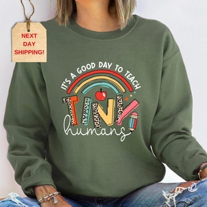 May include: Green sweatshirt with a rainbow and the text "It's a good day to teach tiny humans".