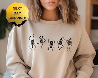 May include: A beige sweatshirt with a graphic of five skeletons dancing. The skeletons are black and are in various poses.