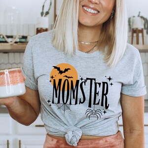 May include: Gray t-shirt with a black and orange graphic design featuring a spider, bats, and the text "MOMSTER".