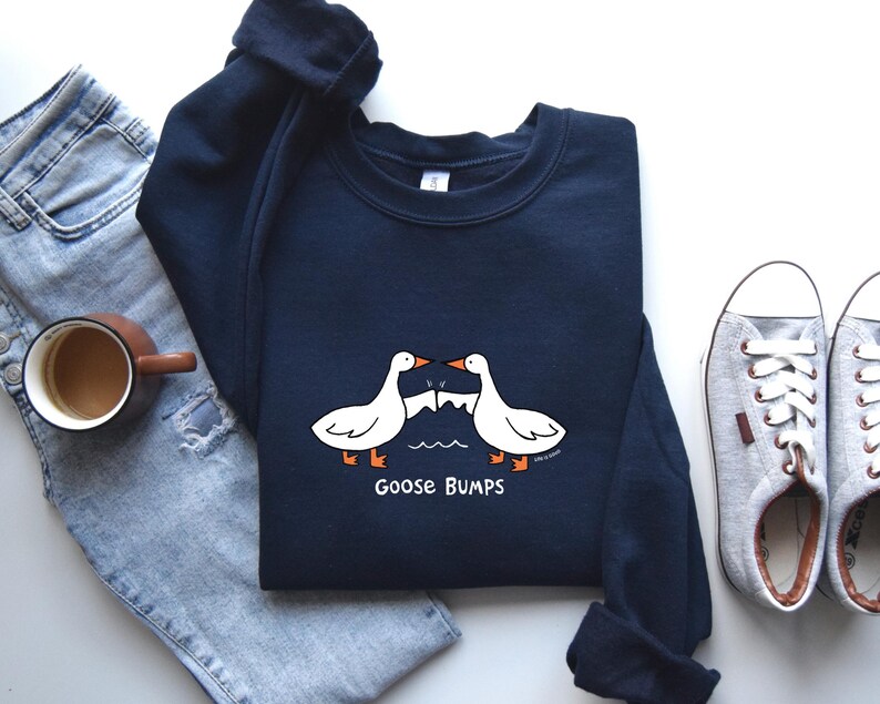 May include: A navy blue sweatshirt with a white graphic of two geese bumping into each other. The text "Goose Bumps" is printed below the geese.