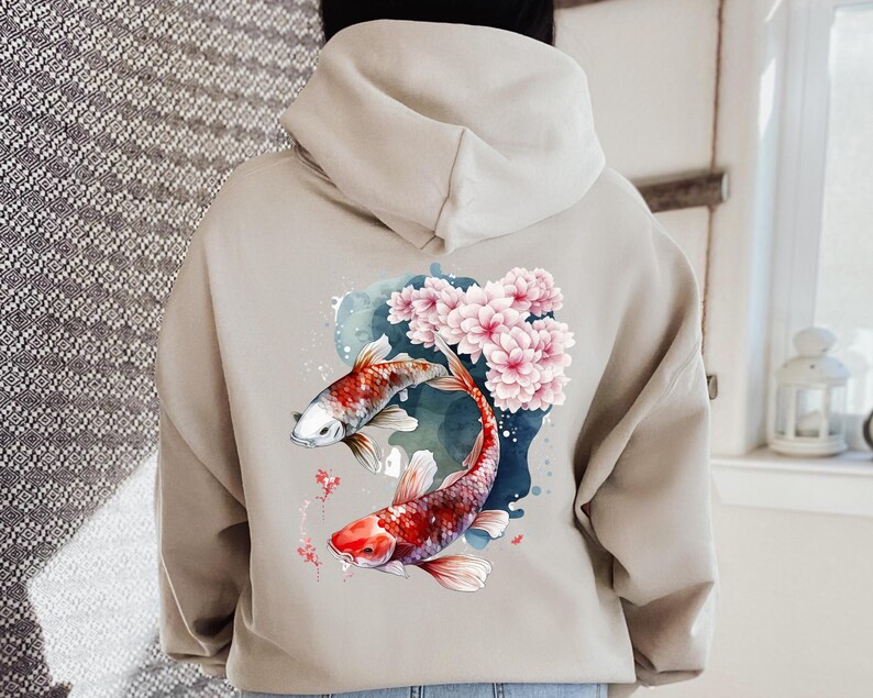 Puede incluir: Una sudadera con capucha beige con un dise&ntilde;o de acuarela de dos peces koi nadando a trav&eacute;s de flores de cerezo rosas.