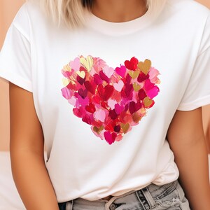 Op de afbeelding: Wit T-shirt met een groot hartontwerp gemaakt van veel kleine roze, rode en gouden hartjes.
