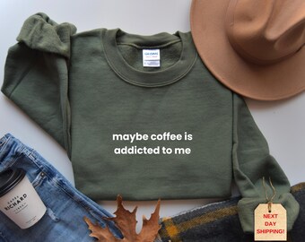 May include: An olive green sweatshirt with the text "maybe coffee is addicted to me" in white. The sweatshirt is laid flat with a brown hat, jeans, and a coffee cup. A tag reads "NEXT DAY SHIPPING!"