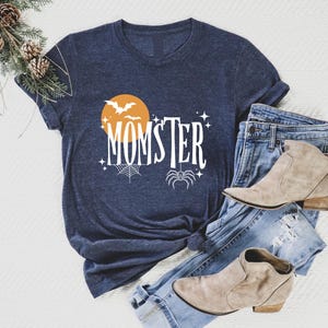 May include: A navy blue t-shirt with a white graphic design featuring a spider, bats, and a moon with the text "MOMSTER".