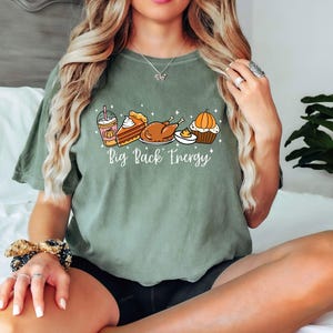 Puede incluir: Camiseta verde salvia con un gr&aacute;fico de alimentos de oto&ntilde;o: un caf&eacute; con leche de calabaza, tarta, pavo y una magdalena. El texto "Big Pack Energy" est&aacute; impreso debajo. La camiseta es de corte holgado.