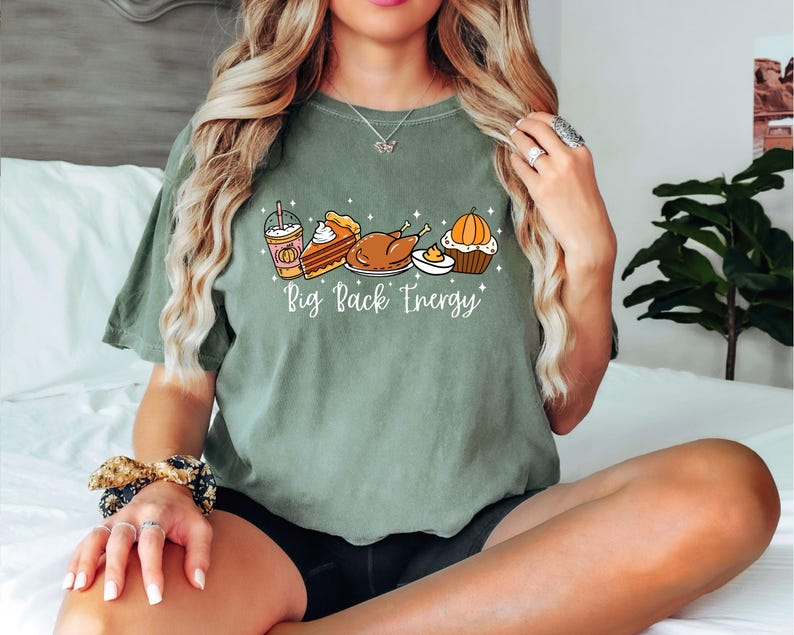 Puede incluir: Camiseta verde salvia con un gr&aacute;fico de alimentos de oto&ntilde;o: un caf&eacute; con leche de calabaza, tarta, pavo y una magdalena. El texto "Big Pack Energy" est&aacute; impreso debajo. La camiseta es de corte holgado.
