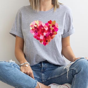 Op de afbeelding: Een grijs T-shirt met een groot hartontwerp gemaakt van kleinere harten in roze en rode tinten.