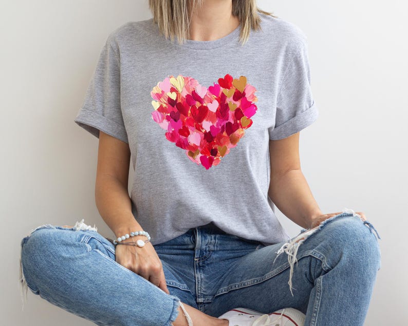 Op de afbeelding: Een grijs T-shirt met een groot hartontwerp gemaakt van kleinere harten in roze en rode tinten.