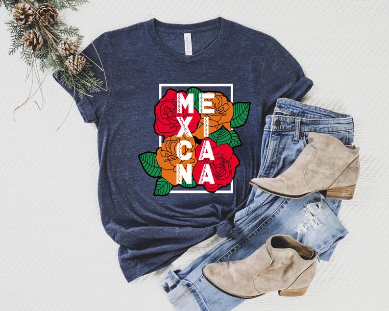 May include: A navy blue t-shirt with the word "MEXICANA" in white letters inside a white rectangle. The design includes red, orange, and yellow roses with green leaves. The shirt is paired with blue jeans and tan ankle boots.