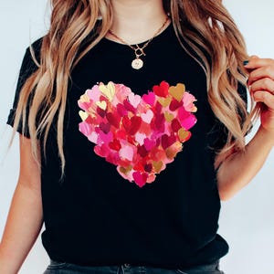 Op de afbeelding: Zwart T-shirt met een groot hartontwerp gemaakt van veel kleinere roze, rode en gouden harten.