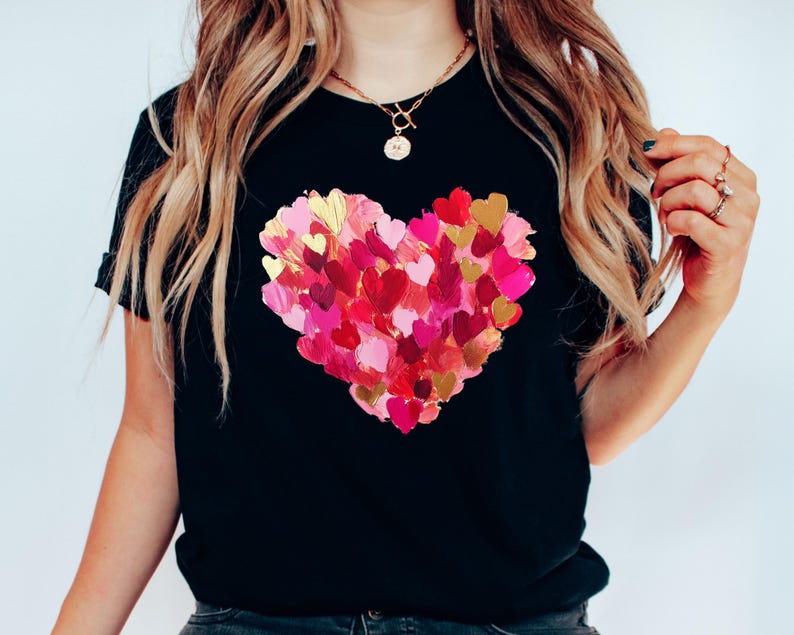 Op de afbeelding: Zwart T-shirt met een groot hartontwerp gemaakt van veel kleinere roze, rode en gouden harten.