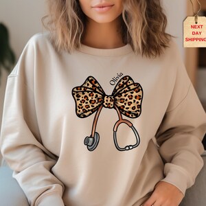 Personalizable Coquette Nurse Sweatshirt & Hoodie, Leopard Print Stethoscope Bow, Sweater Gift for Nurse, Nurse Graduation, Healthcare Tee