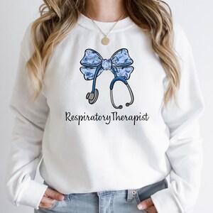 May include: White sweatshirt with a blue and white floral bow and a stethoscope, with the text "Respiratory Therapist" printed below.