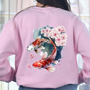 Puede incluir: Sudadera rosa con un dise&ntilde;o de acuarela de dos peces koi nadando a trav&eacute;s de flores de cerezo.