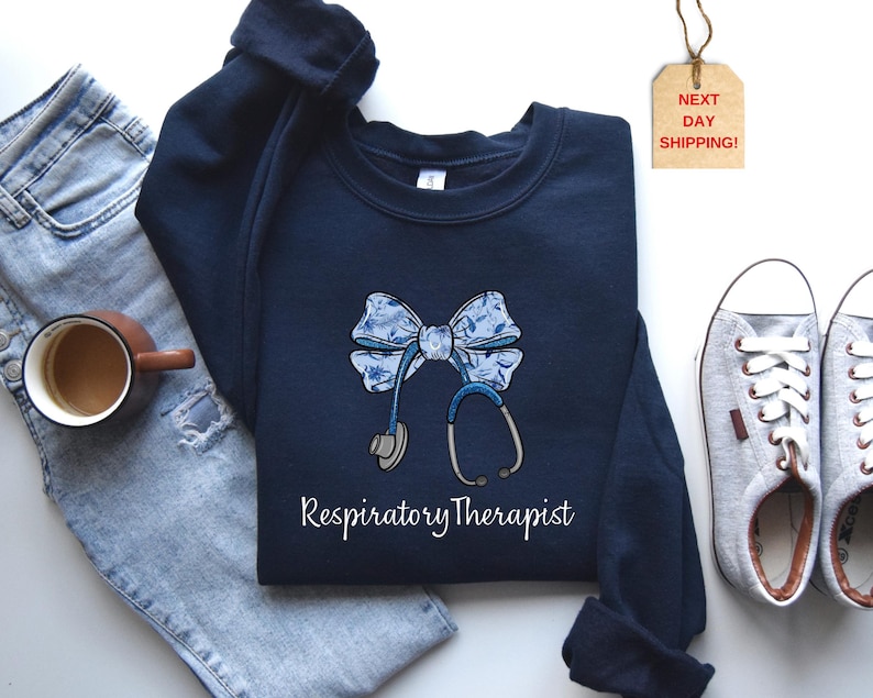 May include: Navy blue sweatshirt with a white and blue bow and stethoscope graphic. The text "Respiratory Therapist" is printed below the graphic.