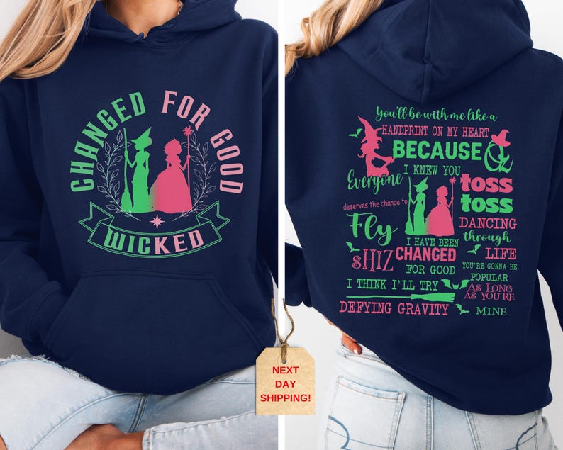 May include: Navy blue hooded sweatshirt with a green and pink graphic of two witches and the text "Changed for Good Wicked". The back of the sweatshirt has a green and pink graphic of a witch and the text "You'll be with me like a handprint on my heart because I knew you everyone deserves the chance to fly toss toss dancing through life I have been shiz changed for good you're gonna be popular as long as you're mine Defying Gravity".