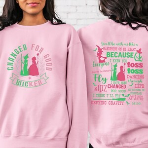 May include: Pink sweatshirt with a green and pink graphic of two witches and the text "Changed for good Wicked". The back of the sweatshirt has a green and pink graphic with the text "You'll be with me like a handprint on my heart because I knew you everyone deserves the chance to fly toss toss dancing through life I have been shiz changed for good you're gonna be popular as long as you're mine Defying Gravity".