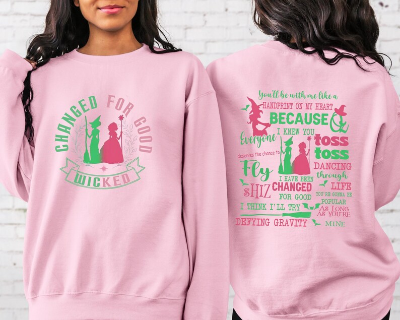 May include: Pink sweatshirt with a green and pink graphic of two witches and the text "Changed for good Wicked". The back of the sweatshirt has a green and pink graphic with the text "You'll be with me like a handprint on my heart because I knew you everyone deserves the chance to fly toss toss dancing through life I have been shiz changed for good you're gonna be popular as long as you're mine Defying Gravity".