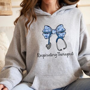 May include: A gray hoodie with a blue floral bow and stethoscope design. The text "Respiratory Therapist" is printed below the design.