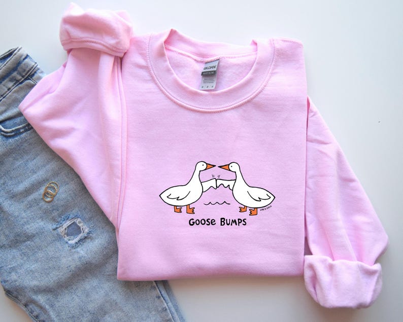 May include: Pink sweatshirt with a graphic of two geese bumping into each other. The text "Goose Bumps" is printed below the geese.