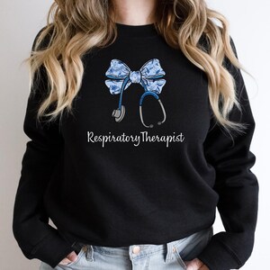 May include: Black sweatshirt with a blue and white bow and a stethoscope, with the text "Respiratory Therapist" printed below.