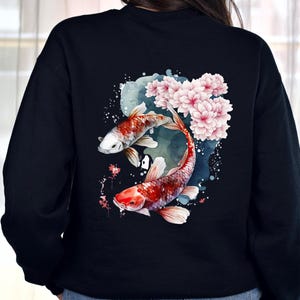 Puede incluir: Sudadera negra con un dise&ntilde;o de acuarela de dos peces koi nadando entre flores de cerezo rosas.
