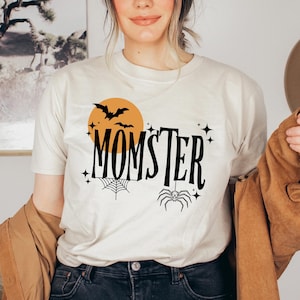 May include: A white t-shirt with a black graphic design that says "Momster" with a spider, bats, and a moon.