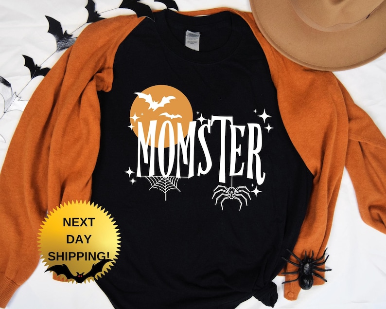 May include: Black and orange long-sleeved shirt with a white graphic of a moon, bats, a spider web, and the text "MOMSTER".