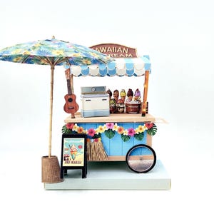 May include: A miniature Hawaiian ice cream cart with a blue and white striped awning, a colorful floral umbrella, and a ukulele. The cart features a sign that reads "Ice Cream". Decorative flowers and a wheel are also visible.