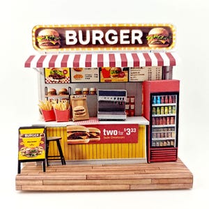 May include: Miniature burger stand with a red and white striped awning. The sign reads "BURGER" with burger illustrations. Includes a menu, fries, a fridge, and a sign that says "two for $333".