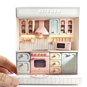 Peut inclure: Un ensemble de jeu de cuisine miniature rose et bleu avec un comptoir blanc, un four rose et un four à micro-ondes. La cuisine porte une pancarte indiquant "Cuisine" au-dessus.