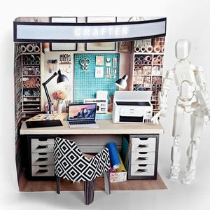 May include: A miniature craft room with a desk, chair, laptop, printer, and shelves filled with supplies. The room is decorated with a sign that says "CRAFTER".