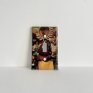 Könnte beinhalten: Ein Lichtschalter-Abdeckung mit einem Vintage-Foto einer Person, die eine Halskette trägt und einen Blumenstrauß hält.