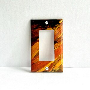 Könnte beinhalten: Dekorative einzelne Lichtschalterabdeckung mit einem lebendigen abstrakten Design. Die Abdeckung hat eine rechteckige Öffnung und ist mit einer Mischung aus Orange-, Gelb- und Brauntönen verziert, die mit zwei Schrauben befestigt sind. Maße: ca. 11,4 cm x 7,6 cm.