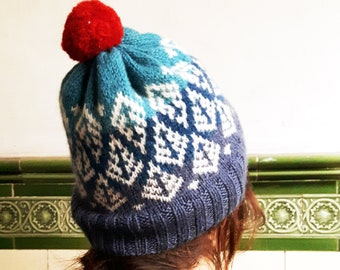 Hand knit Fair Isle hat design in blue, with bold tree motif and red pom pom