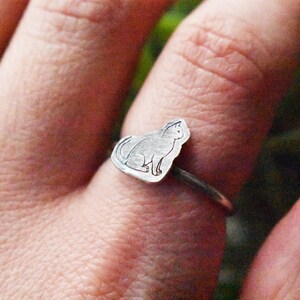 May include: A silver ring featuring a cat silhouette design. The ring is worn on a person's finger.