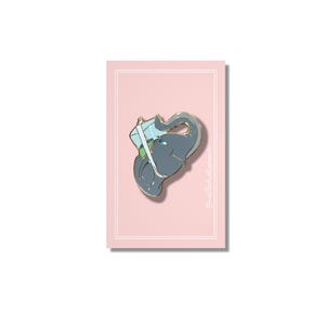 May include: A gray elephant enamel pin with gold trim, carrying a light blue package. The pin is set against a pink background with a white border. The pin is a cute and whimsical accessory.