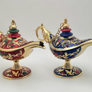 Puede incluir: Dos lámparas de genio adornadas con detalles dorados y diseños intrincados. Una lámpara es roja con detalles verdes, y la otra es azul con detalles dorados.